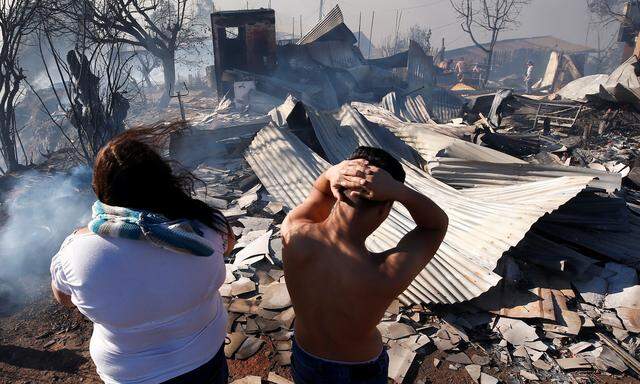 A woman and her son react next to the debris of their house as a fire continues in Valparaiso
