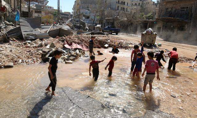 Children play with water from a burst water pipe at a site hit yesterday by an air strike in Aleppo's rebel-controlled al-Mashad neighbourhood
