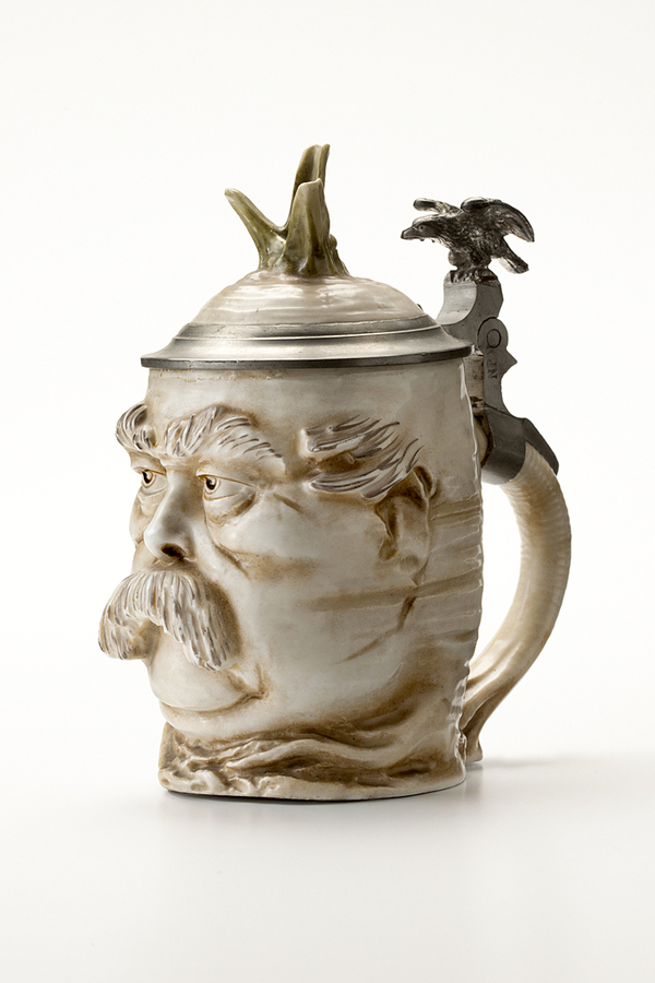 Es folgen weitere Ausstellungsstücke aus "Böse Dinge. Eine Enzyklopädie des Ungeschmacks": Bierkrug in Form eines Rettichs mit Bismarck-Gesicht Porzellanmanufaktur Schierholz & Sohn, C.G., Deutschland, 1890.