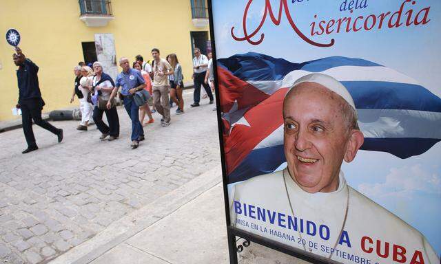 Tourists pass by a poster with a photograph of Pope Francis with the message in Spanish that reads ´Welcome to Cuba´ in Havana