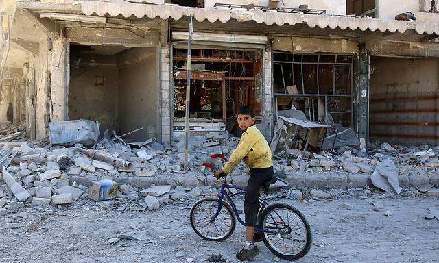 A boy sits on a bicycle in front of damaged shops after an airstrike on the rebel held al-Qaterji neighbourhood of Aleppo