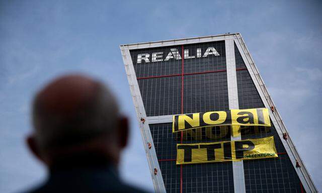 A man looks at Greenpeace activists displaying a banner against TTIP free trade agreement while suspended on one of the Kio towers in Madrid