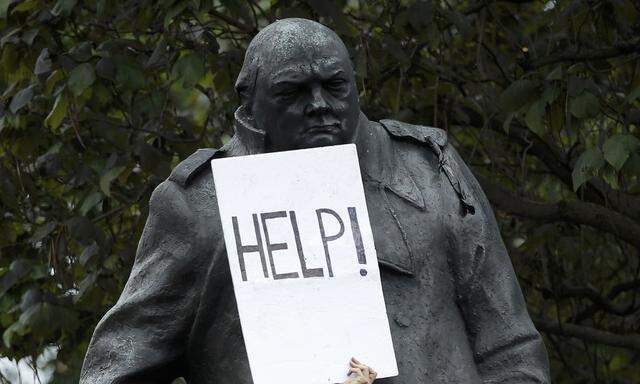 A demonstrator holds a placard that reads 'Help!' against a statue of Winston Churchill during an anti-austerity protest in central London