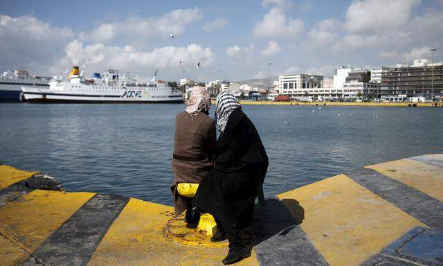Two stranded migrants sit at a pier at the port of Piraeus, near Athens