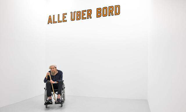 Lawrence Weiner bei einem seiner letzten Wien-Besuche 2018 in der Galerie Hubert Winter. Hinter ihm eine seiner Wortskulpturen.