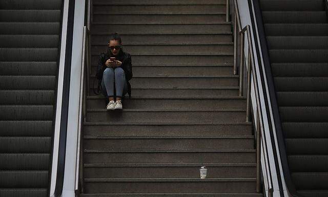A woman uses her mobile phone as she sits on the stairs at Principe Pio station in Madrid