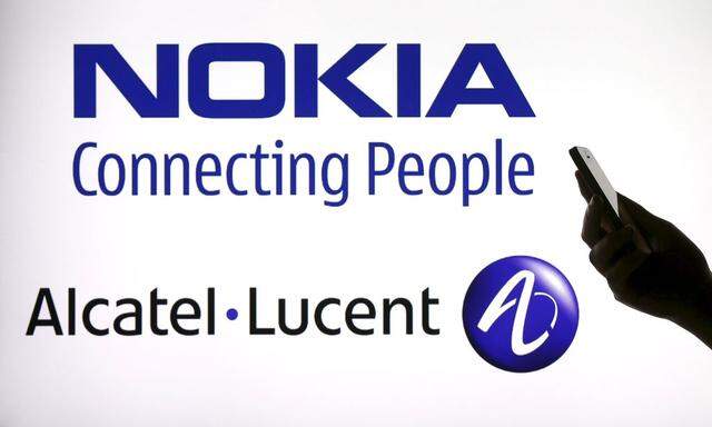 File photo illustration of a woman holding a smartphone in front of a screen displaying both Nokia and Alcatel Lucent logos in Paris