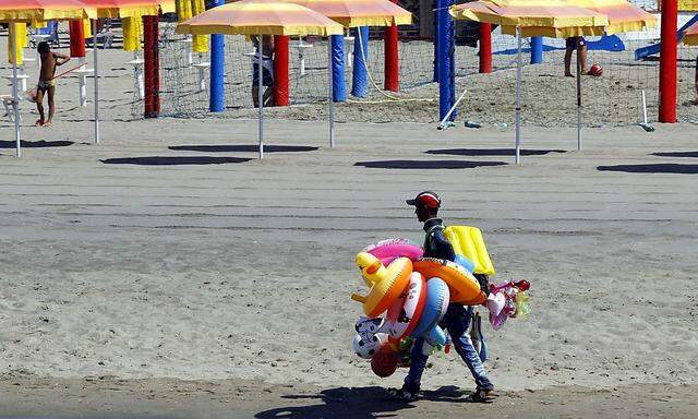 A man carries inflatable toys for sale on an empty beach during a hot summer day in Ostia, near Rome