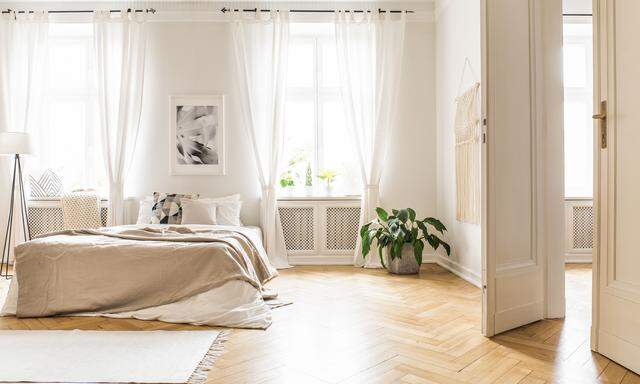 Spacious and bright bedroom interior with beige decorations, hardwood floor and a book on the window sill seat