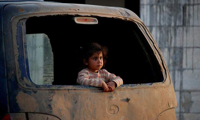 An internally displaced Syrian girl inspects the area from a broken window of a van in an IDP camp located near Idlib