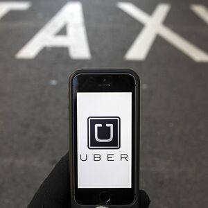 Photo illustration of logo of car-sharing service app Uber on a smartphone over a reserved lane for taxis in a street in Madrid