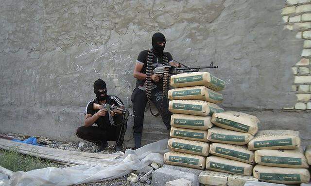 Masked gunmen hold their weapons as they take positions during a patrol outside the city of Falluja