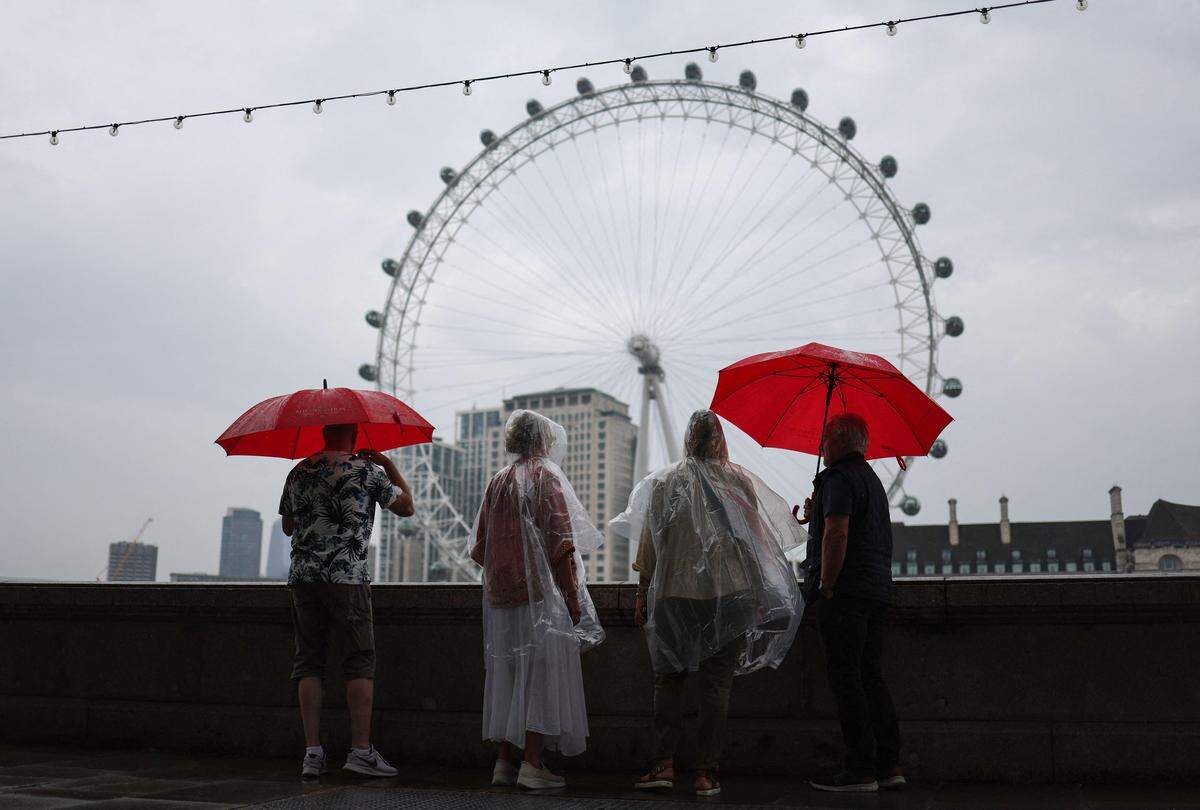 18. August. Fußgänger schützen sich vor dem Regen an einem trüben Sommertag an der Themse im Zentrum Londons.