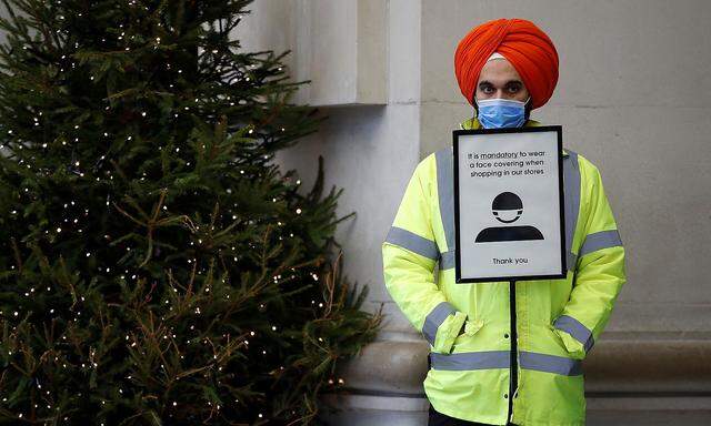 A security guard stands by a sign asking customers to wear face masks at a store in London
