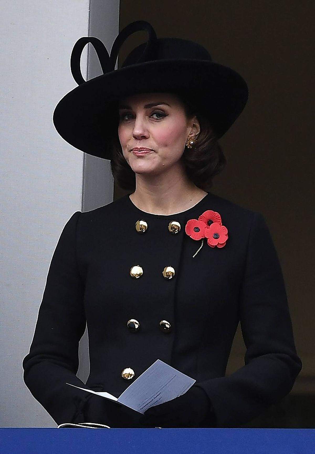 Das alljährliche Soldatengedenken beim Londoner Außenministerium Mitte November lässt den Royals kaum Spielraum bei der Auswahl ihrer Outfits. Wer nicht Uniform trägt (oder tragen kann), kommt in Schwarz, die Gedenkabzeichen - die roten Mohnblumen - müssen ohnehin mit von der Partie sein. Kate entschied sich für eine Mischung der zwei Stilvorgaben und erschien in einem taillierten Mantel von Dolce & Gabbana - mit glänzenden Knöpfen in Goldoptik. Auch ein zweites neues Stück führte die Herzogin aus: eine schwarze Clutch mit Goldrand vom britischen Label Emmy.