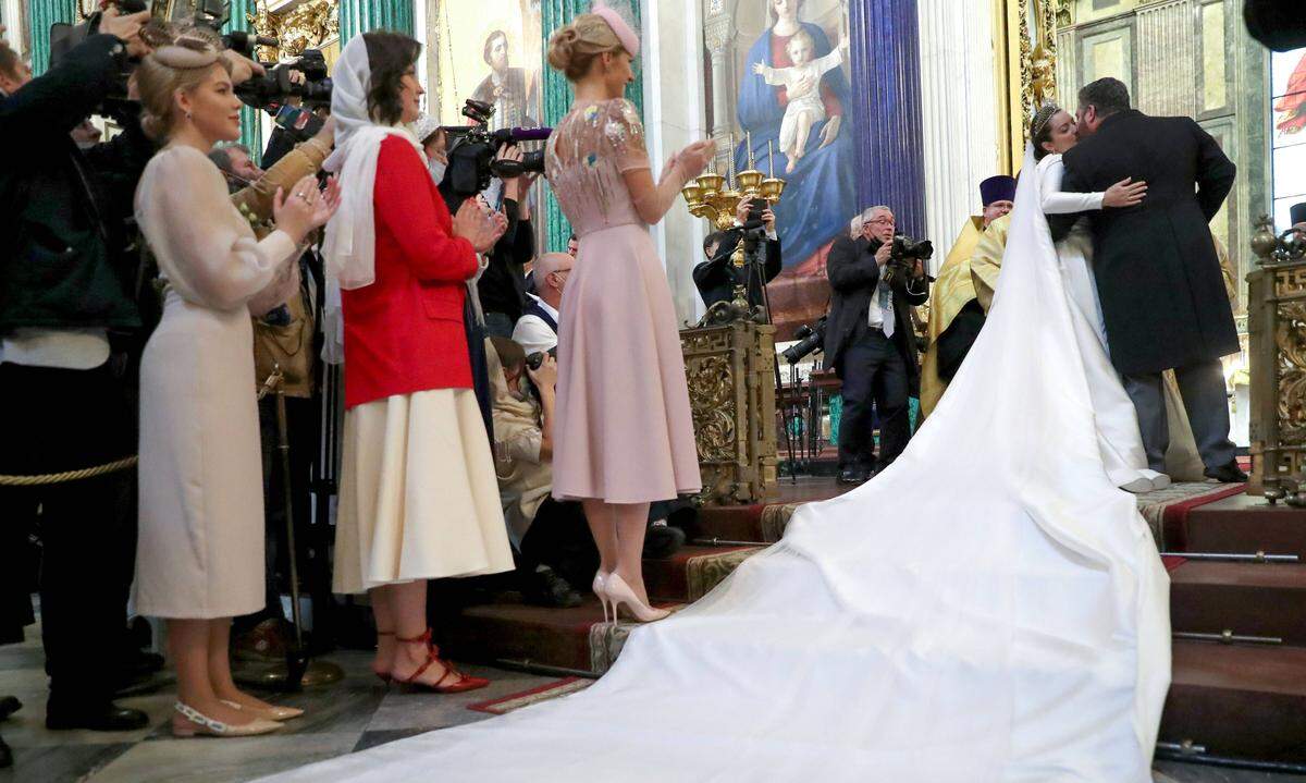 Die Braut trug ein langes weißes Kleid mit dem in Goldfaden gestickten Wappen des russischen Reichs sowie eine meterlange Schleppe. Entworfen hat es die russische Designerin Elina Samarina.
