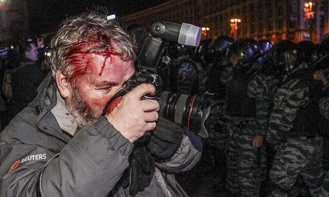 Wounded Reuters photographer takes pictures as riot police block protesters during a scuffle at a demonstration in support of EU integration at Independence Square in Kiev