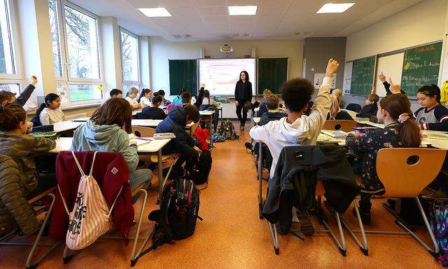 Students raise their hands during a lesson with geography teacher Dinar Pamukci at Hesse's largest high school, Karl-Rehbein-Schule