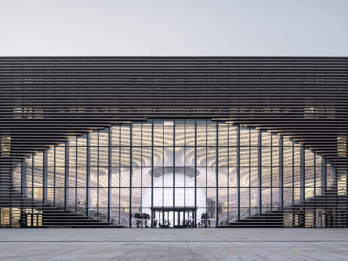 Tianjin Binhai Bibliothek im chinesischen Binhai wurde von MVRDV entworfen. Das 33.700 Quadratmeter große Kulturzentrum verfügt über ein kugelförmiges Auditorium um das raumhohe Bücherregale kaskadieren.       