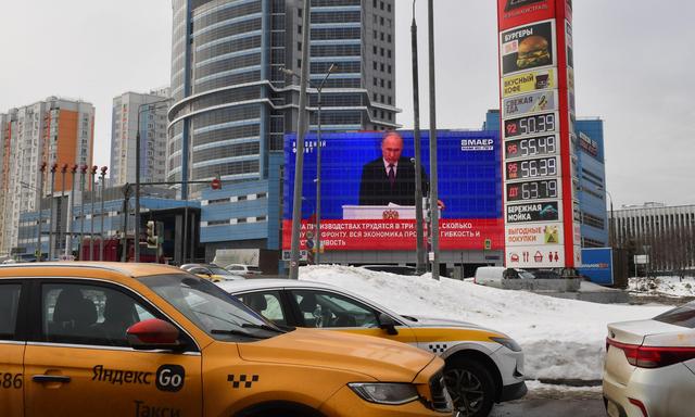 Autos auf Moskaus Straßen. Im Hintergrund läuft eine TV-Übertragung von Wladimir Putins Rede vor der Föderalen Versammlung.