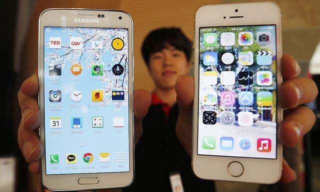 A sales assistant holding Samsung Electronics´ Galaxy 5 smartphone and Apple Inc´s iPhone 5 smartphone poses for photographs at a store in Seoul