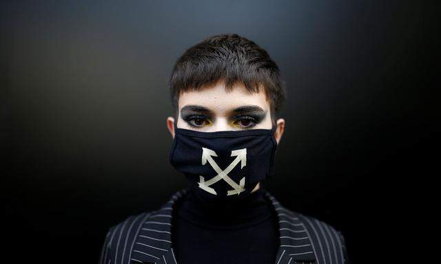 Man wearing a face mask poses outside of a venue at London Fashion Week in London