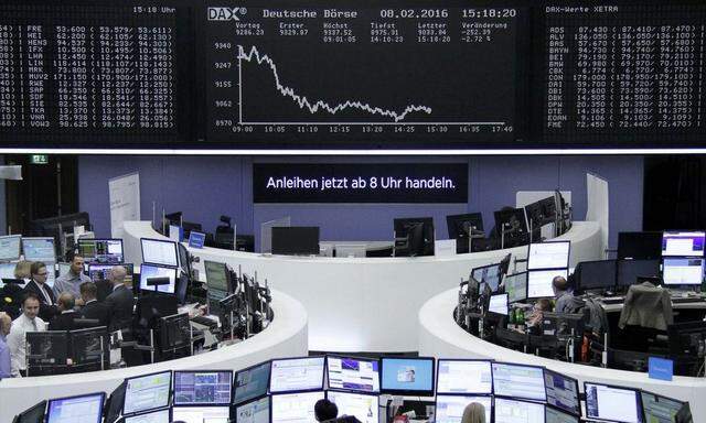 Traders work at their desks in front of the German share price index, DAX board, at the stock exchange in Frankfurt