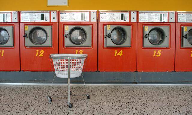 Ein leerer Wäschekorb steht vor mehreren Waschmaschinen in einem Waschsalon.