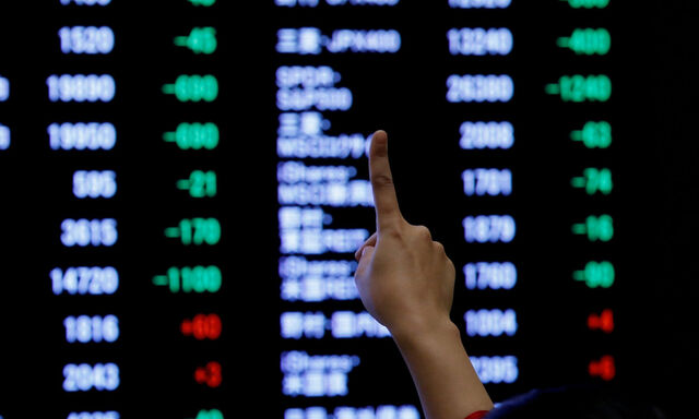 FILE PHOTO: A woman points to an electronic board showing stock prices as she poses in front of the board after the New Year opening ceremony at the Tokyo Stock Exchange (TSE), held to wish for the success of Japan's stock market, in Tokyo