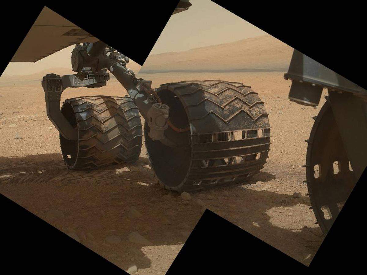 Die "Curiosity" ist mit sechs Rädern ausgestattet, im Bild die linke Seite. Im Hintergrund ist der Mount Sharp zu sehen, zu dem der Rover letztendlich fahren soll.