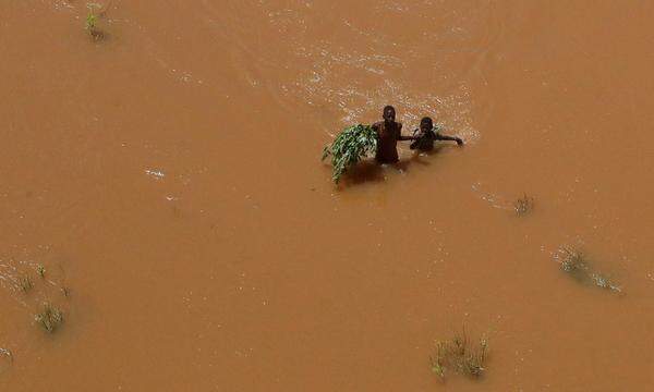Menschen halten sich an Pflanzen fest, während sie durch das Hochwasser waten, nachdem sie nach heftigen Regenfällen in Garsen im kenianischen Tana-Delta am 23. November 2023 vertrieben wurden.