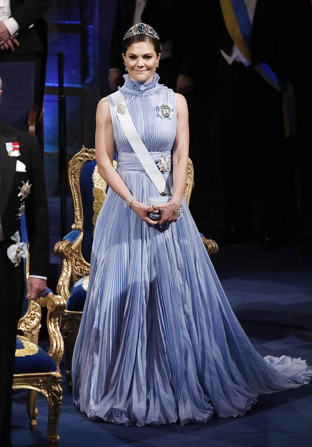 Kronprinzessin Victoria hatte bei der Nobel-Gala aber in ihrer Robe von Jennifer Blom ohnehin den großen Auftritt gebucht. Das fliederfarbene plissierte Kleid mit hohem Kragen passt tadellos in die Reihe dramatischer Outfits, die Victoria traditionellerweise zu dem Anlass wählt.