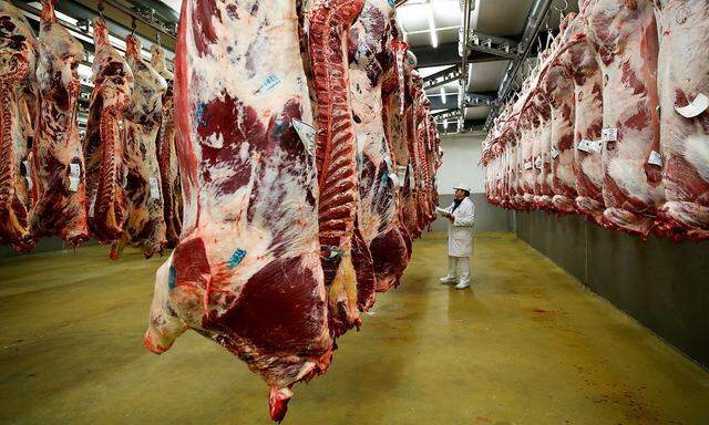 FILE PHOTO: A wholesaler inspects beef carcasses that hang inside a refrigerated room at the Cibevial slaughterhouse in Corbas