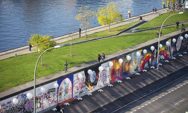 People walk under stands with balloons placed along the former Berlin Wall location at East Side Gallery in Berlin