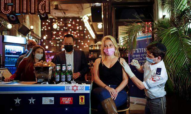 FILE PHOTO: A woman receives a vaccination shot against the coronavirus disease (COVID-19) as part of a Tel Aviv municipality initiative offering a free drink at a bar to residents getting the shot, in Tel Aviv