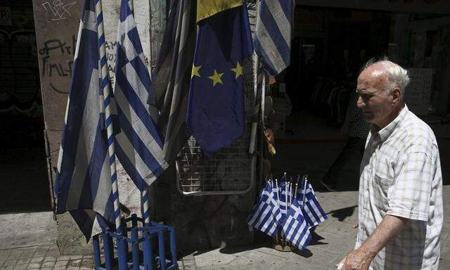 A man walks past Greek national flags and European Union flags on display outside a shop in central Athens