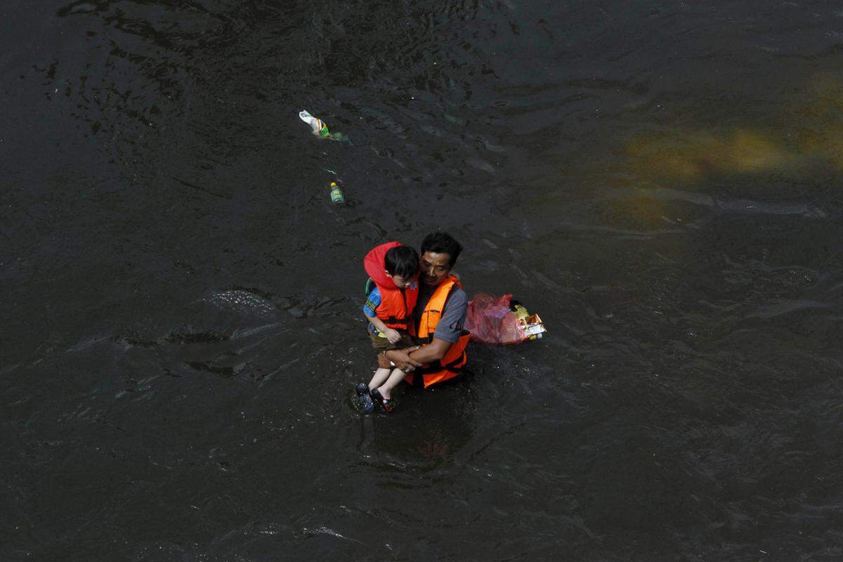 In der Provinz Pathum Thani vor Bangkok bringt ein Mann seinen Sohn aus den Fluten in Sicherheit.