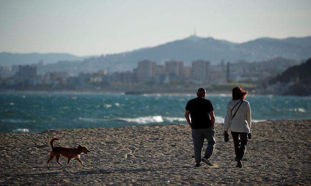 A couple walks with a dog on a beach following the coronavirus disease (COVID-19) outbreak in El Masnou