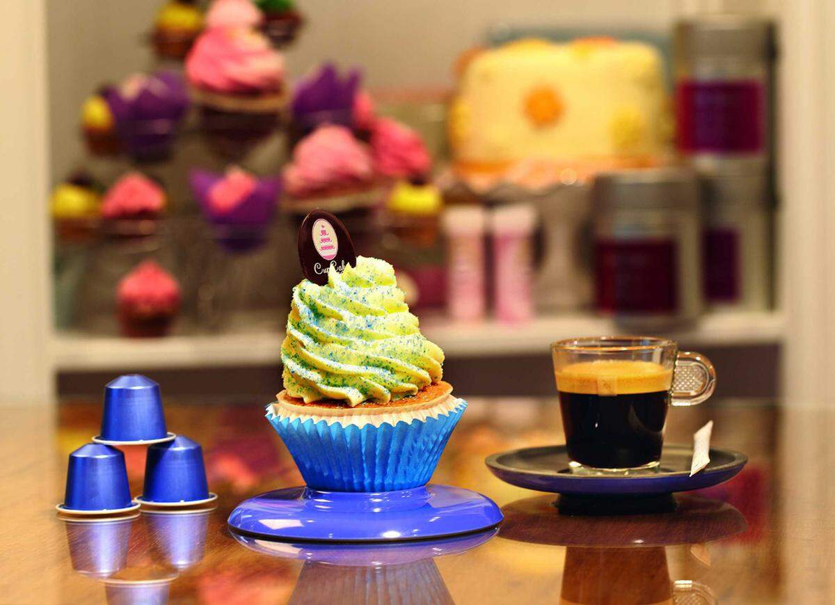 Zutaten Schokoladen-Kaffee-Sponge: 130 g Haushaltsschokolade 140 g zimmerwarme Butter 110 g Staubzucker Mark einer Vanilleschote 2 Kapseln Nespresso Ristretto 6 Eidotter 6 Eiklar 110 g Kristallzucker 140 g Mehl, glatt Zutaten blauer Zucker: 2 EL grober Kristallzucker 1 Pkg. blaue Lebensmittelfarbe aus der Apotheke 1 TL Zitronensaft oder Blue Curacao (für eine leicht säuerliche Note) Zutaten Bananen-Topping: 1 Becher Mascarino (500 g) 1 Becher Topfen (250 g, 20% Fett, streichfähig, kein Bröseltopfen) 2 mittelgroße, reife Bananen 2 EL Zitronensaft Staubzucker nach Geschmack zum Süßen Zubereitung: Am Vortag den blauen Zucker für das Topping vorbereiten. Hierzu den Zucker, die Farbe und den Zitronensaft oder Blue Curacao mit einander verrühren, den Zucker auf Backpapier auftragen und über Nacht trocknen lassen. Für den Schokoladen-Kaffee-Sponge die Haushaltsschokolade klein hacken und im Wasserbad schmelzen. Die handwarme Butter, den Staubzucker, das Vanillemark und die 6 Eidotter auf höchster Stufe für ca. 5 Minuten verrühren. Aus den beiden Nespresso Ristretto Kapseln einen Espresso (je 25 ml) herstellen und mit der geschmolzenen Schokolade in die Masse einlaufen lassen. 6 Eiklar mit Kristallzucker steif schlagen und mit einem Kochlöffel vorsichtig unter die Butter-Ei-Masse heben. Zum Schluss das Mehl in die Masse einrühren und in Muffin-Förmchen füllen. Für das Bananen-Topping eine ganze und eine halbe Banane mit etwas Zitronensaft pürieren. Die übrige halbe Banane in Scheiben schneiden, mit Zitronensaft beträufeln, damit sie sich nicht braun färbt und beiseite stellen. Den Topfen mit Mascarino und Staubzucker in einer Schüssel mixen, das Bananenpüree beimengen und in einen Spritzbeutel mit Sterntülle (Durchmesser ca. 2 cm) füllen. In runden Kreisbewegungen auf den Schokoladen-Kaffee-Sponge aufdressieren. Zum Schluss den blauen Zucker auf das Topping aufstreuen, den Cupcake mit 2 Bananenscheiben verzieren und genießen! (Ergibt ca. 12 bis 14 Stück.)Alle Rezepte von Cupcakes Wien.