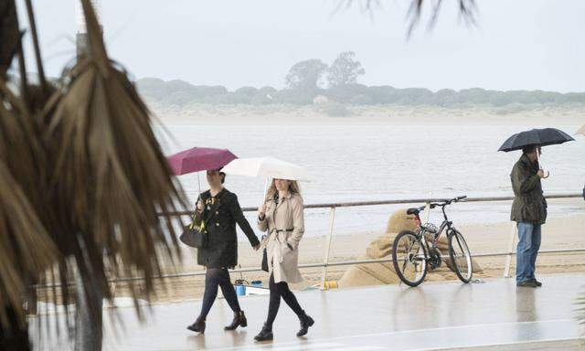 Leute spazieren im Regen auf der Promenade an der Mündung des Guadalquivir.