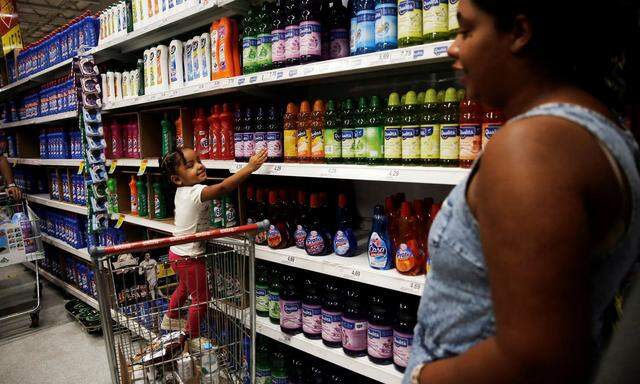 Child stands on a shopping cart as she points at cleaning products next to her mother at a supermarket in Sao Paulo