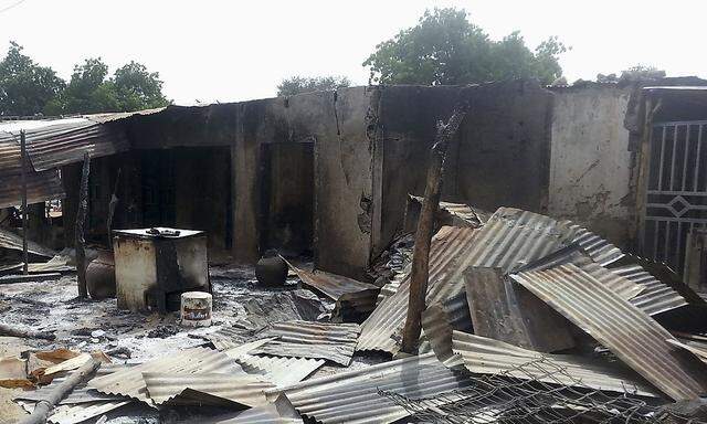 Residents stand in front of destroyed properties and houses following an attack in Kawuri