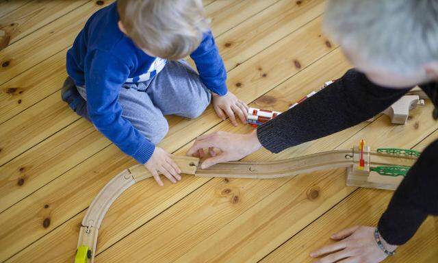 Symbolfoto: Ein Kleinkind und eine Frau spielen auf dem Fussboden mit einer Holzeisenbahn