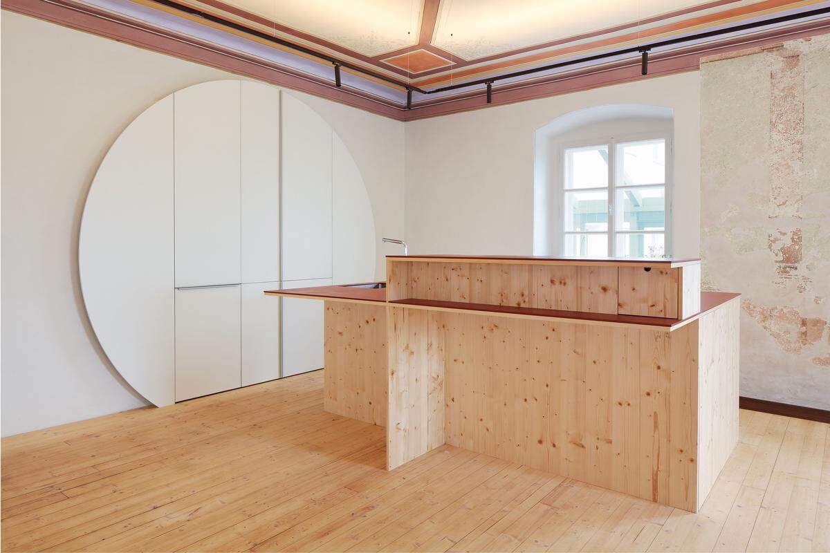 Der in die Wand eingelassene Schrank wird durch die aufgesetzte kreisrunde Front zur geometrischen Ergänzung für den kantigen Küchenblock.
