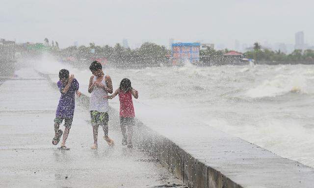 TOPSHOT - Children walk along a sea wall at Navotas in Metro Manila on July 26, 2023, as Super Typhoon Doksuri passes close to the northern tip of Luzon island. (Photo by JAM STA ROSA / AFP)