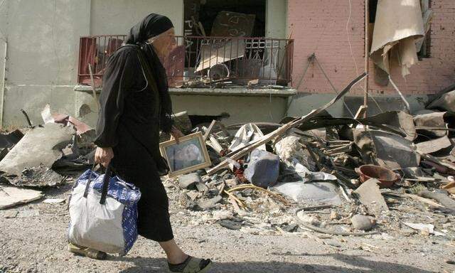 A Georgian woman carries her belongings from her damaged home in Gori