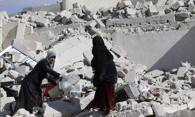 Women hold plastic bottles as they stand amid rubble of damaged buildings at a site in Masaken Hanano in Aleppo
