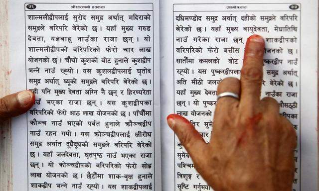 A Hindu holy man holds the holy book on his hand as he recites verses from the Swasthani Brata Katha book at the bank of River Saali in Sankhu during the first day of Swasthani Brata Katha festival in Kathmandu