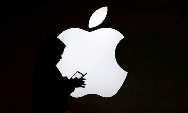 A woman looks at the screen of her mobile phone in front of an Apple logo outside its store in Shanghai