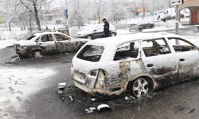 A policeman investigates a burnt car in the Rinkeby suburb outside Stockholm